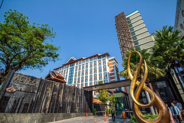 A hotel entrance with a prominent sign, a modern building in the background, and a large abstract sculpture.