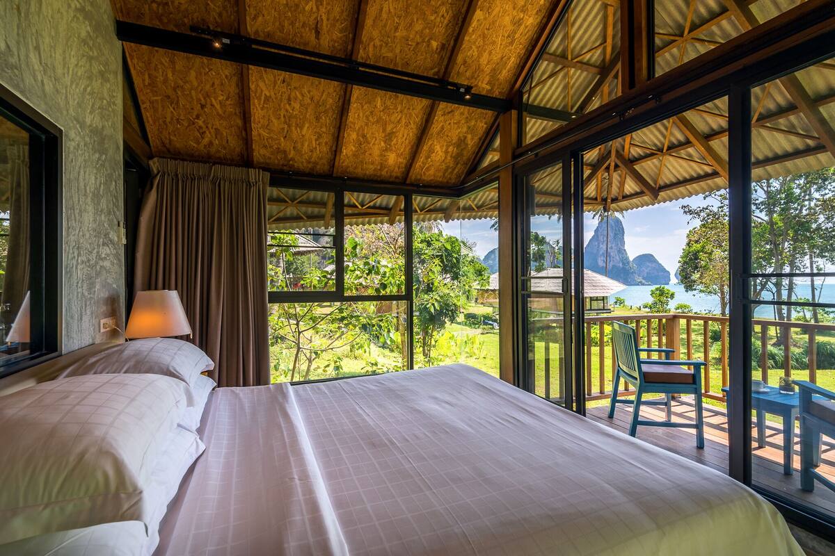 Un dormitorio con una cama grande, vistas al exterior y un balcón con una silla y una mesa.