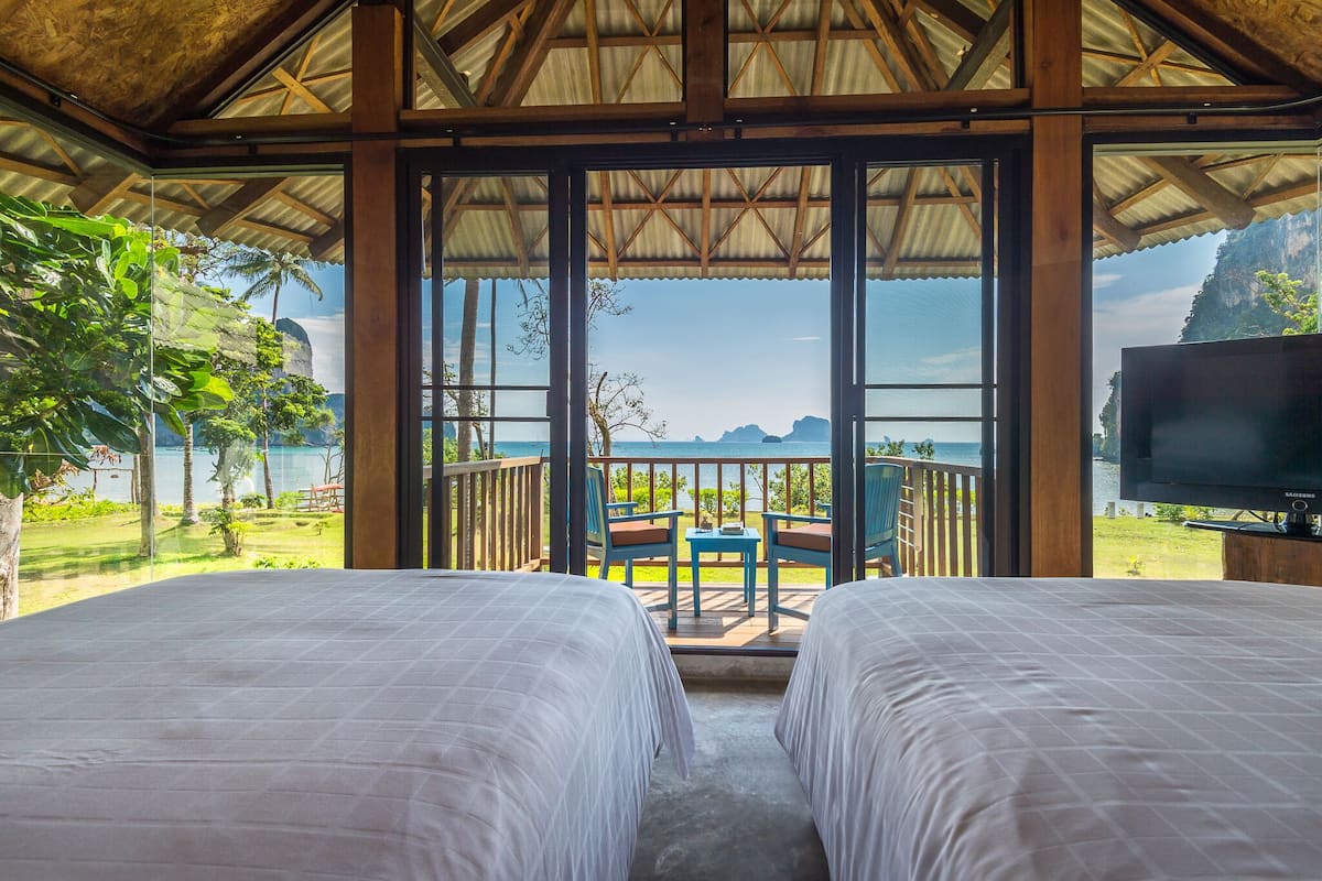 Habitación con dos camas, televisor y balcón con vista al mar y a las montañas.