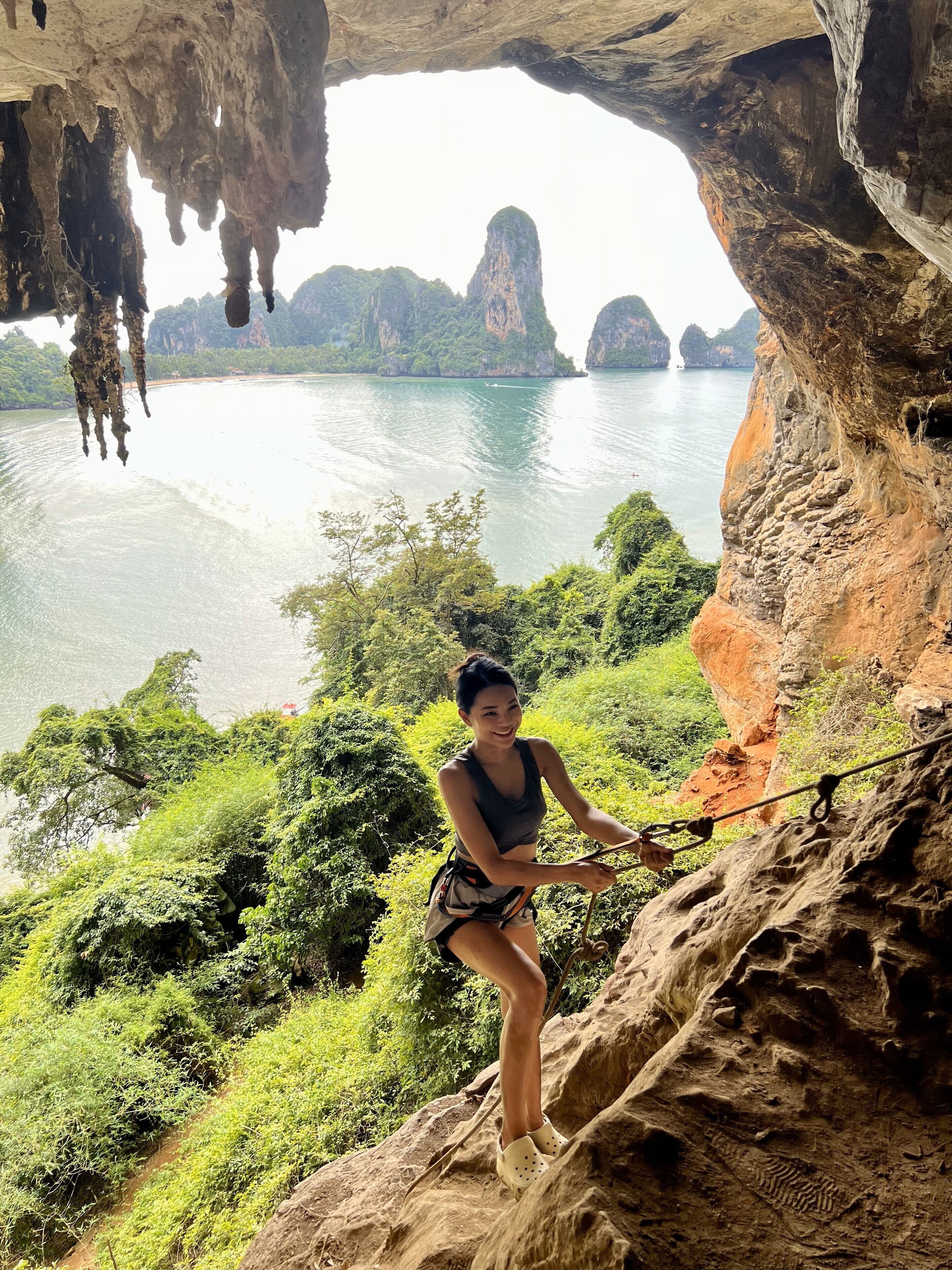 A person rappelling down a rocky cliff with a view of a river and distant mountains.