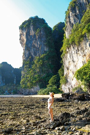 A rocky beach with a person standing near the water, cliffs in the background, and a clear sky.