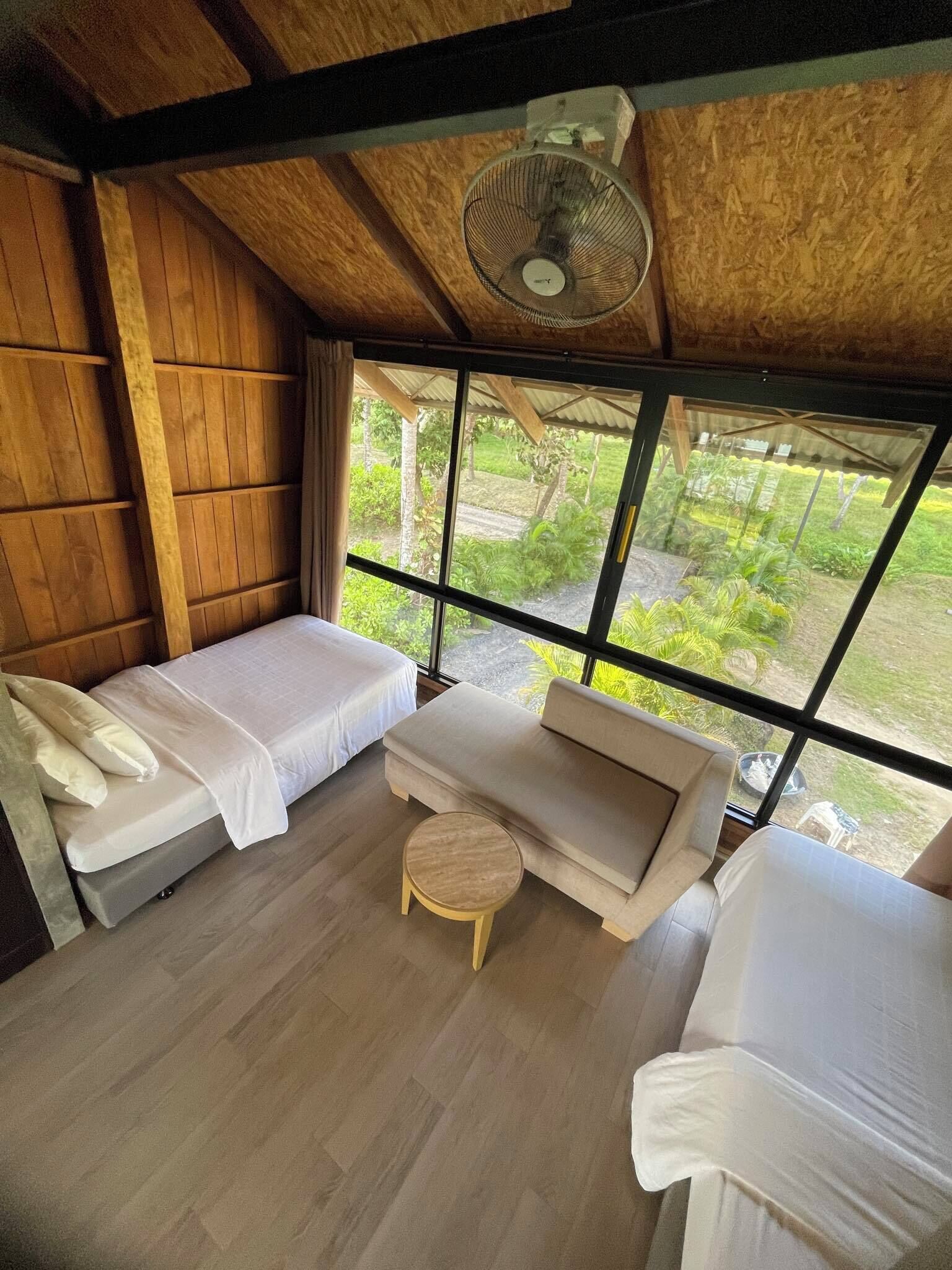 A room with two beds, a sofa, a small round table, and a ceiling fan.