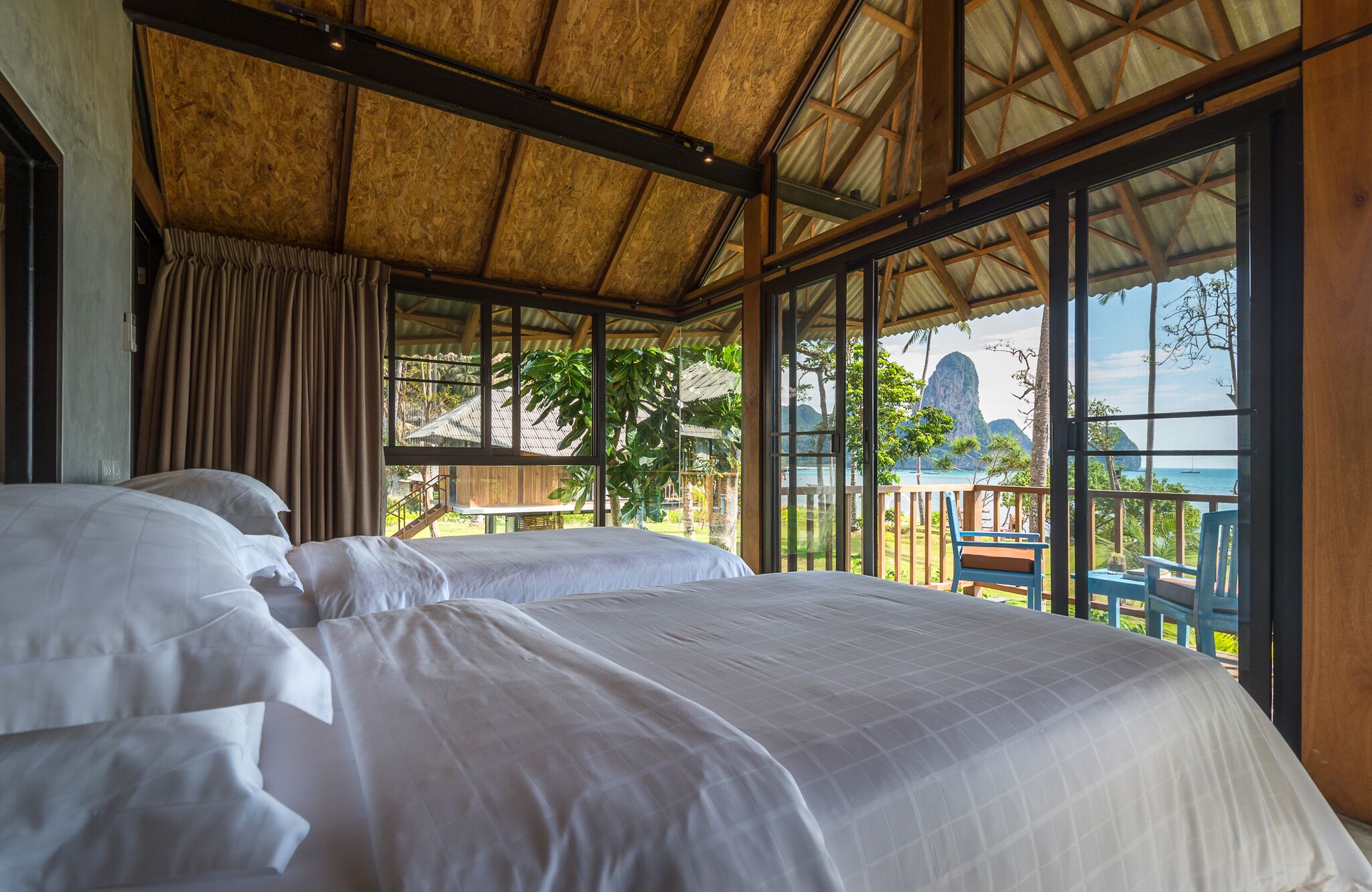 A bedroom with a large bed, a view of the sea, and a balcony with a chair.