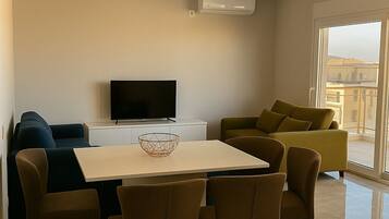 A modern living room with a dining table, chairs, a sofa, and a TV.