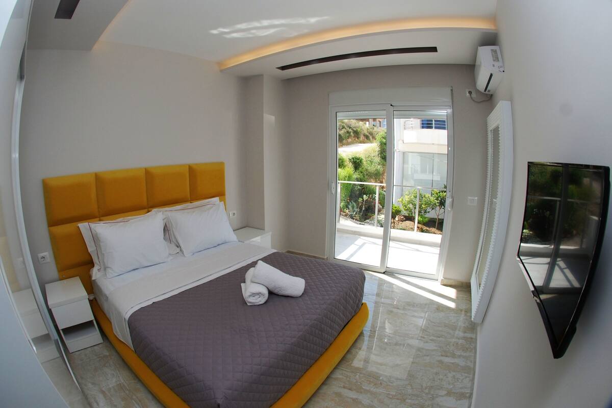 A modern bedroom with a bed, a nightstand, a TV, and a balcony with a view.