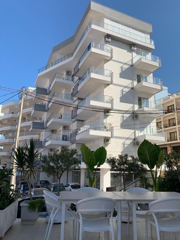 Un edificio residencial de varios pisos con balcones, rodeado de automóviles estacionados y plantas en macetas.