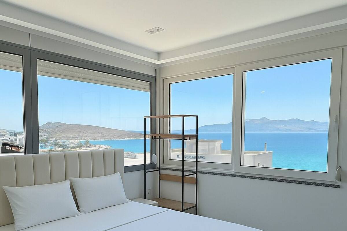 A modern bedroom with a large bed, a view of the sea, and a balcony with a railing.