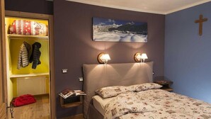 Un dormitorio con cama, lámparas de noche, mesita de noche, estantería y una cruz colgada en la pared.