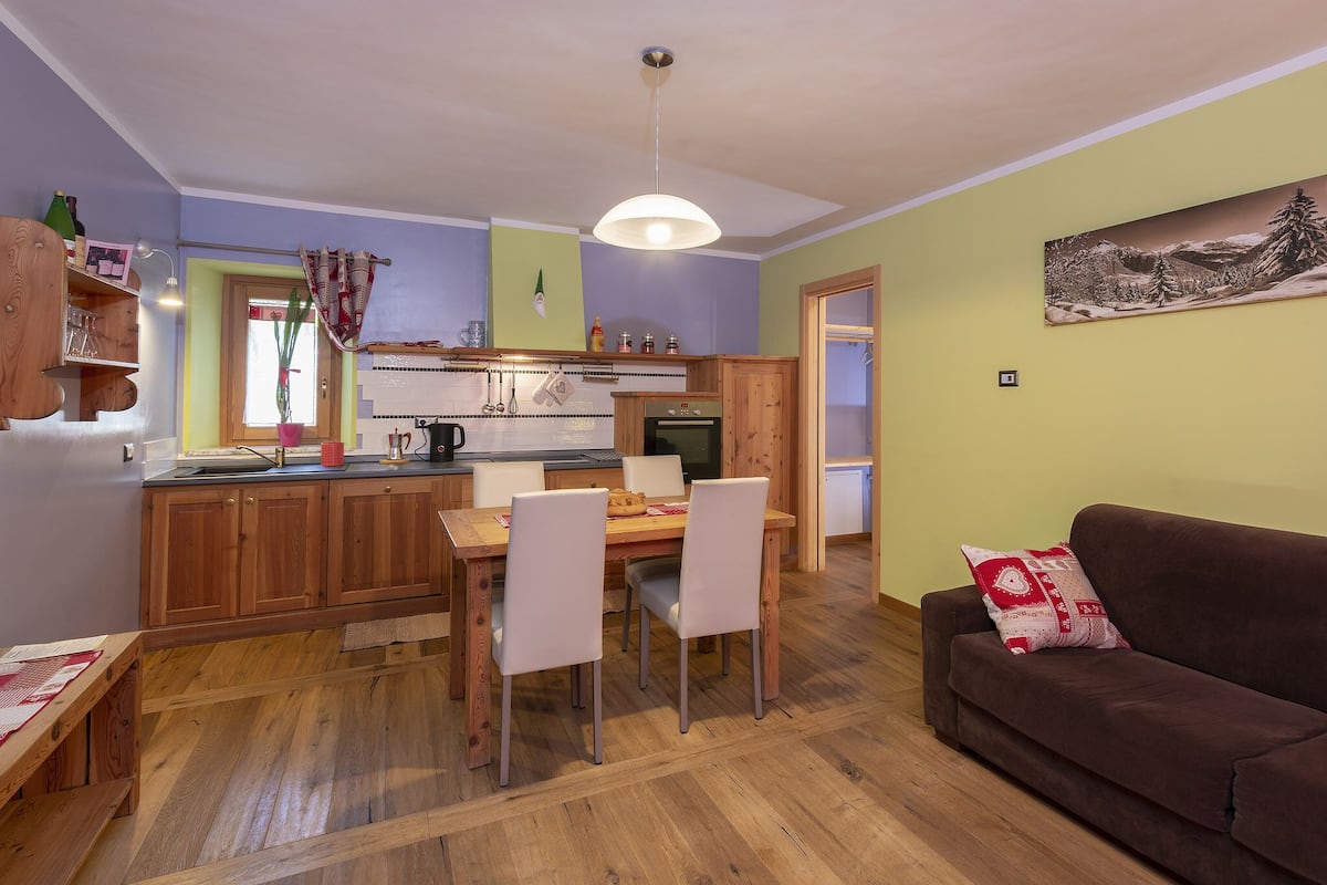 Eine gemütliche Küche mit Holzschränken, einem Esstisch mit Stühlen und einem braunen Sofa.