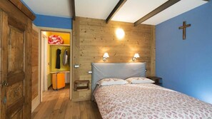 A bedroom with a wooden headboard, a bed with patterned bedding, a nightstand with two wall-mounted lamps, a wooden wardrobe, and a cross on the wall. - Agriturismo Gli Elfi (Saint-Christophe)