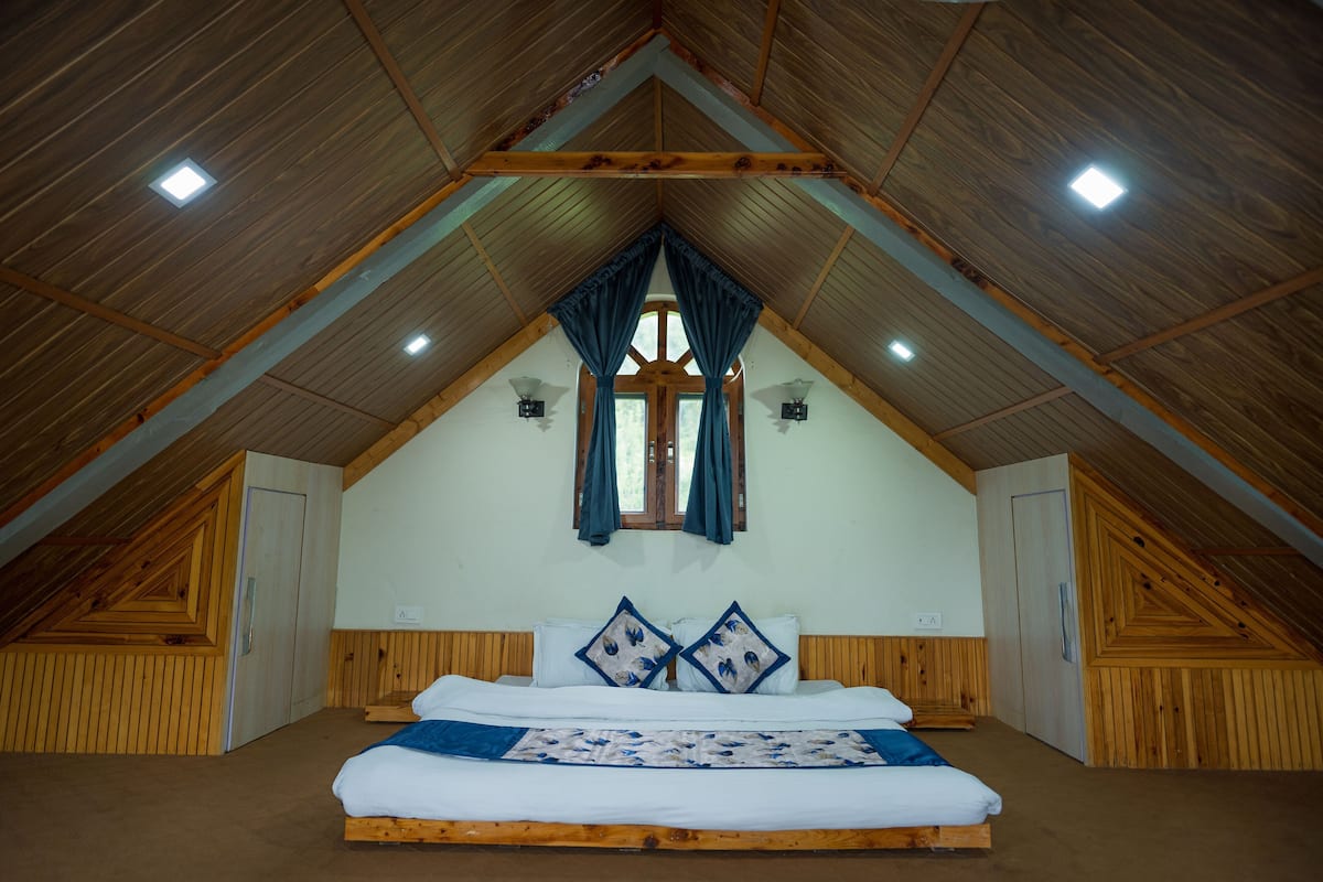 Un dormitorio con techo de madera, cama con ropa de cama blanca y ventana con cortinas.