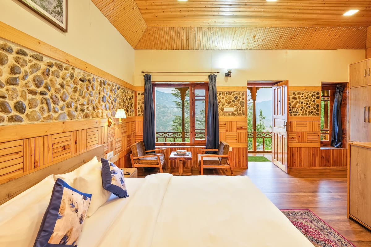 Una cabaña de madera con pared de piedra, cama con almohadas, mesa con sillas y vista a las montañas.