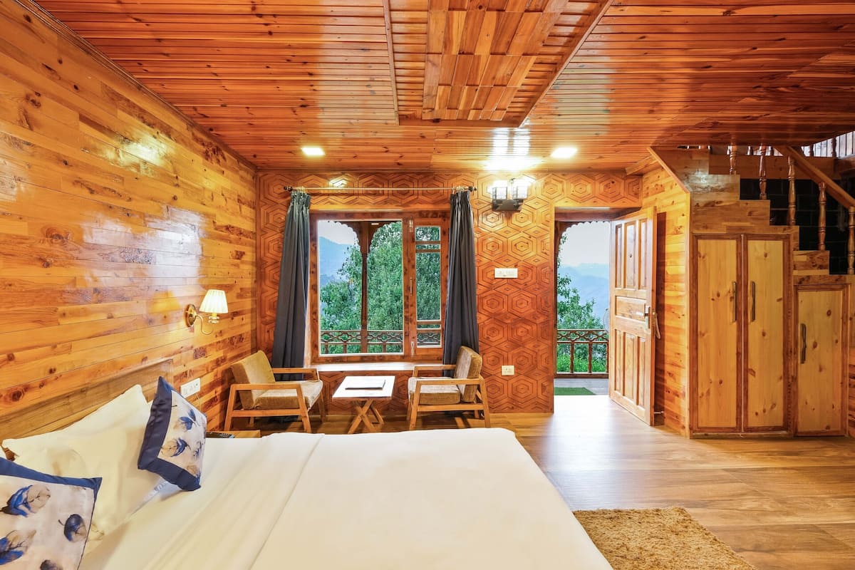 Una habitación de cabaña de madera con una cama, dos sillas, una mesita y vistas al exterior.