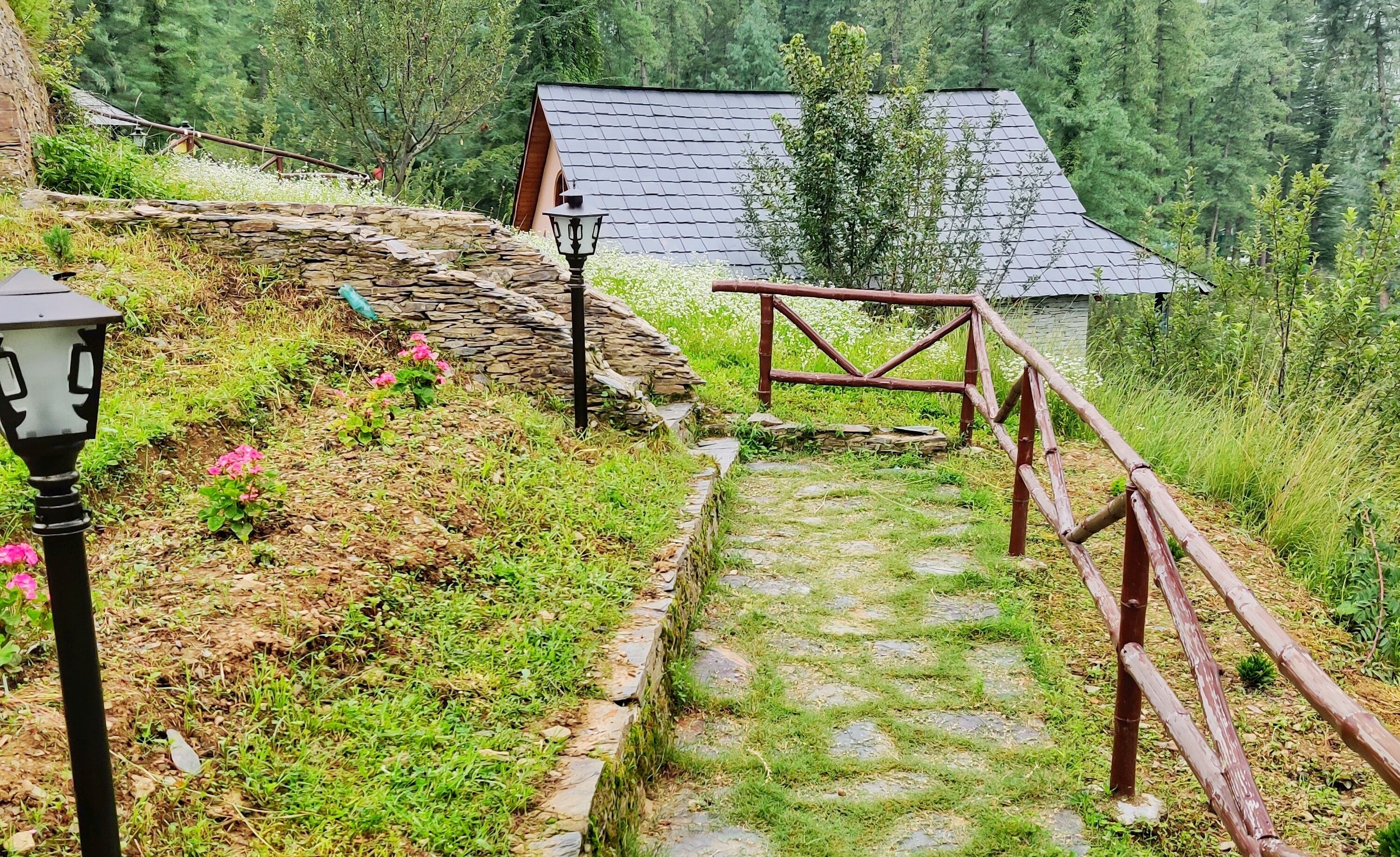 Un sendero de piedra que conduce a un edificio rústico con barandilla de madera y un farol.