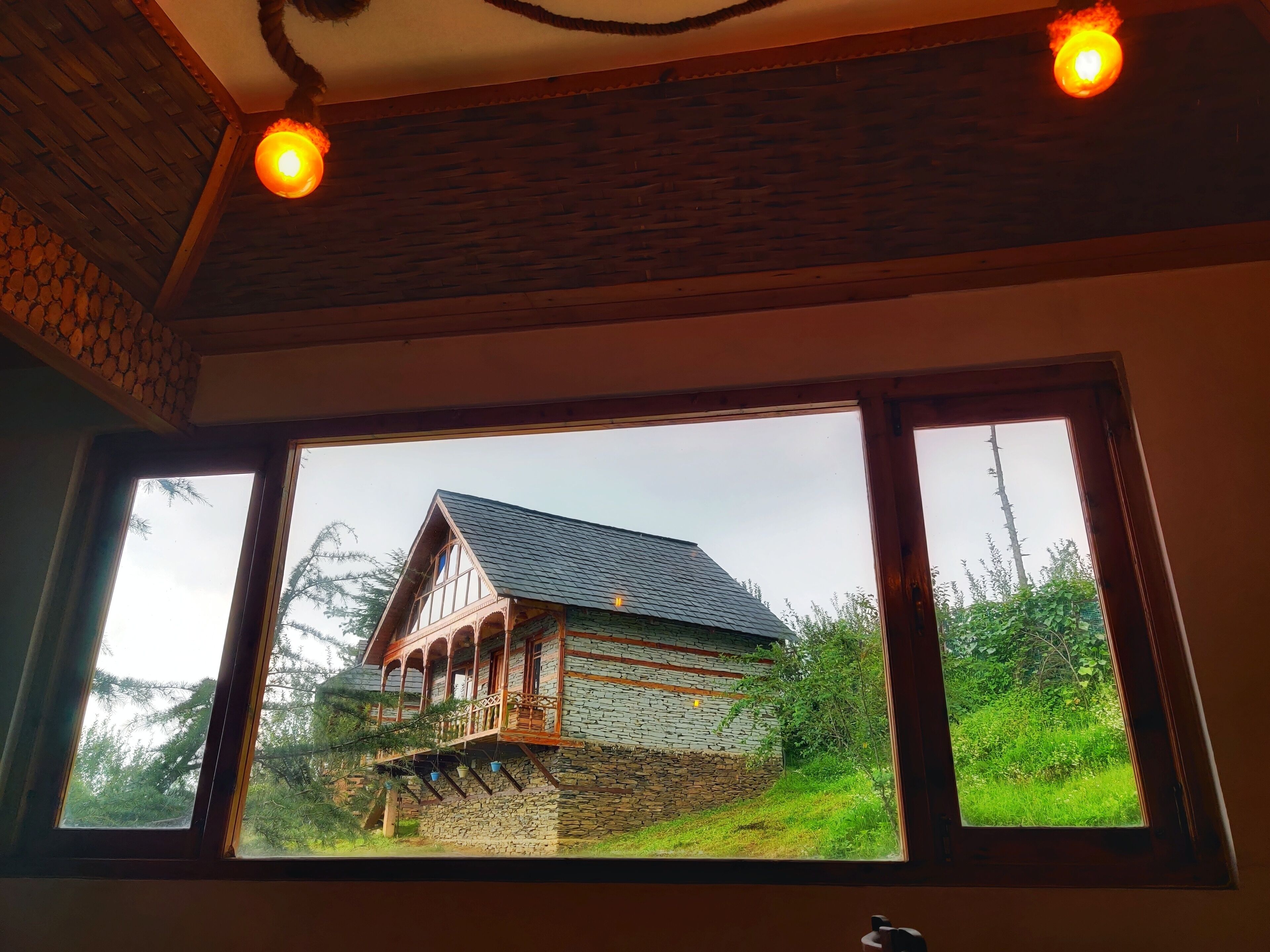 Et værelse med et stort vindue, der kigger ud på et hus med en murstenssokkel og en træbalkon.