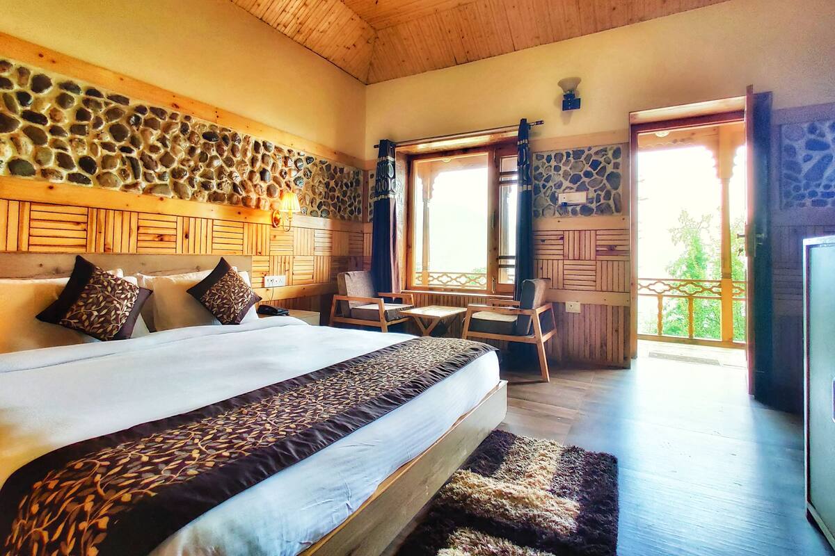 Un dormitorio con cama, escritorio y silla, pared de piedra y techo de madera.
