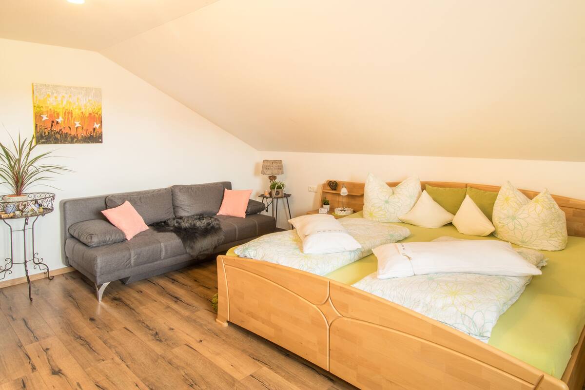 A bedroom with a wooden bed, a grey sofa, and a small table with a lamp.
