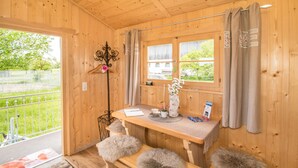 A wooden cabin interior with a wooden table, bench, and a view of a green landscape through a window. - Ferienparadies Reifnhof (Riedering)