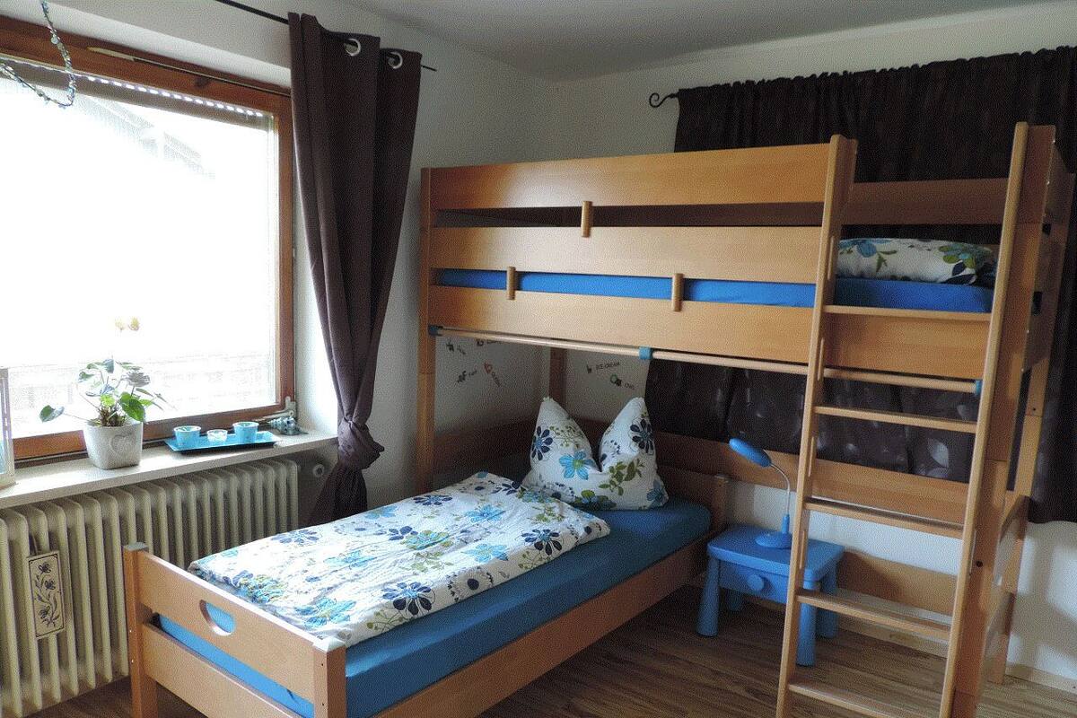 A bunk bed with a wooden frame, a small table, and a potted plant by the window.