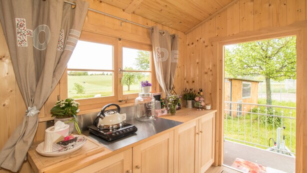 A wooden cabin kitchen with a stove, tea set, and potted plants. - Ferienparadies Reifnhof (Riedering)