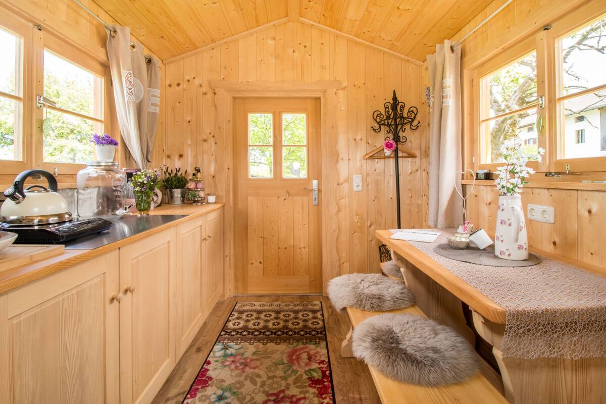 A wooden cabin interior with a kitchen area, wooden cabinets, a door with windows, and a hanging light fixture.