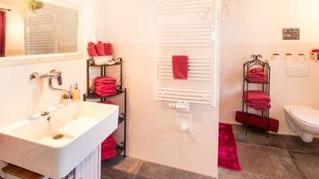Une salle de bain avec un lavabo blanc, un miroir, un porte-serviettes, des toilettes et un espace douche.