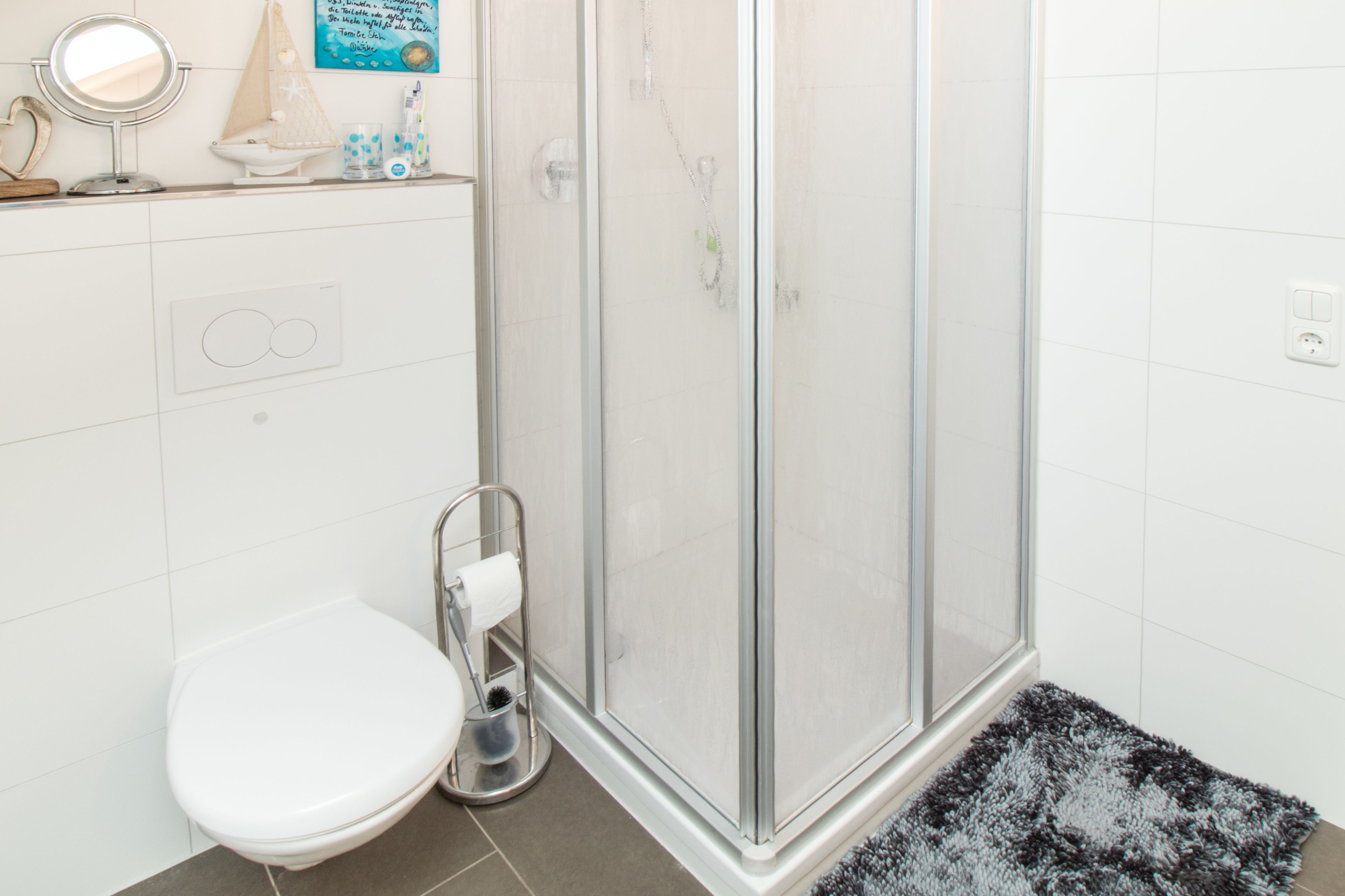 Un baño con inodoro, cabina de ducha de vidrio y una alfombra pequeña.