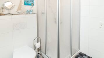 Un baño con inodoro, cabina de ducha de vidrio y una alfombra pequeña.