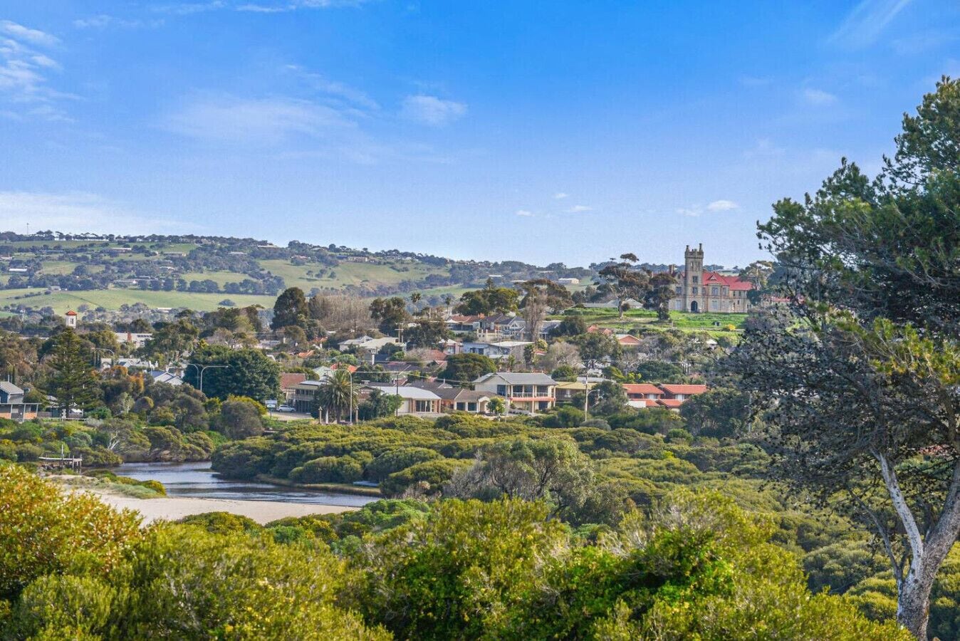 A coastal town with a prominent tower, lush greenery, and a river.