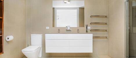 Een moderne badkamer met een wit toilet, een ruime wastafel met spiegel en een douchecabine van glas.
