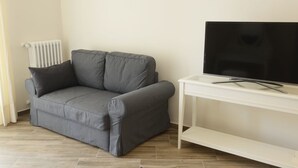 A grey sofa, a white TV stand, and a radiator in a room with wooden flooring. - B&B Fronte del Porto (Salerno)