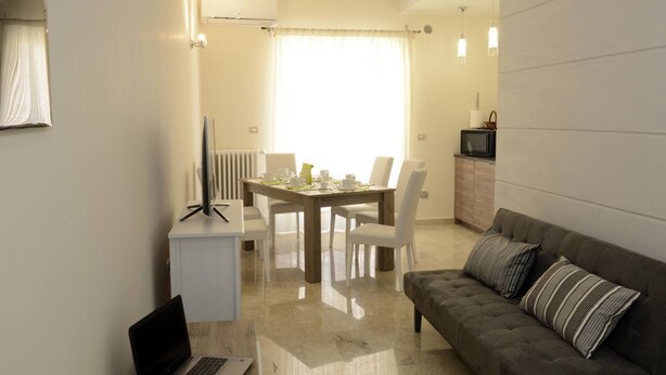 A modern living room with a dining area, a sofa, a TV, and a laptop on a desk. - B&B Fronte del Porto (Salerno)