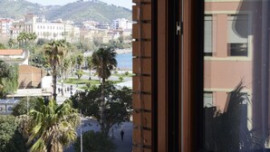 A view from a window overlooking a cityscape with palm trees, a body of water, and buildings. - B&B Fronte del Porto (Salerno)