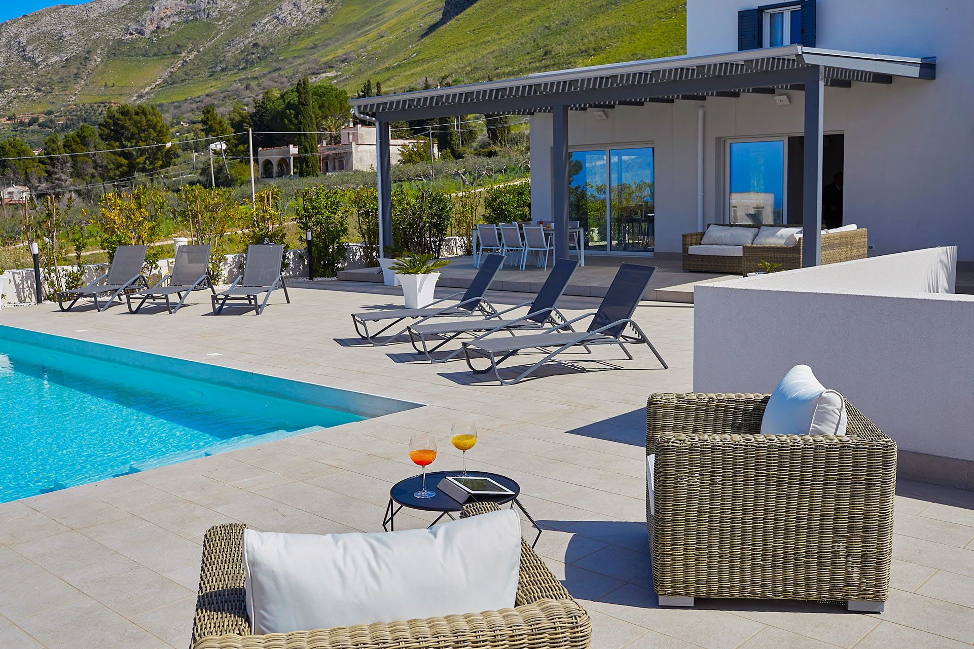 A poolside area with lounge chairs, a table with drinks, and a view of a mountain.