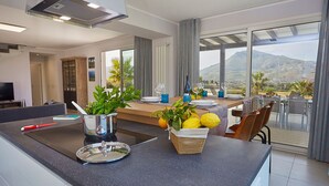 A modern kitchen with a central island, dining area with a view, and a large window overlooking a mountainous landscape.
