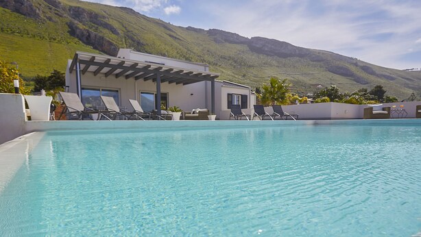 A pool area with lounge chairs and a building with a pergola.