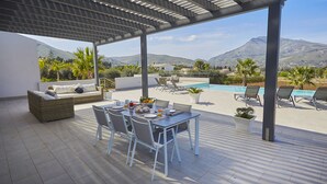 An outdoor patio with a table, chairs, a sofa, and a pool.
