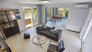 A modern living room with a grey sofa, a leather armchair, a glass coffee table, and a TV stand.