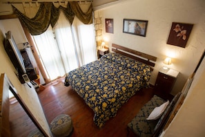 A bedroom with a large bed, two bedside tables with lamps, a wooden bench, a small rug, and a mirror on the wall.