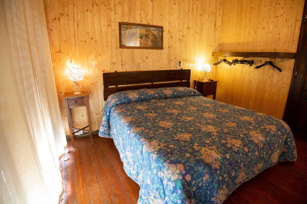 Un dormitorio con paredes de madera, una cama con colcha estampada, dos lámparas de noche y un cabecero de madera.