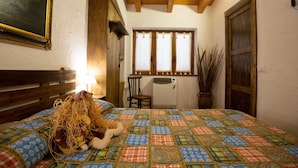 Un dormitorio con cabecera de madera, edredón acolchado de colores, una puerta de madera rústica y una ventana con cortinas.