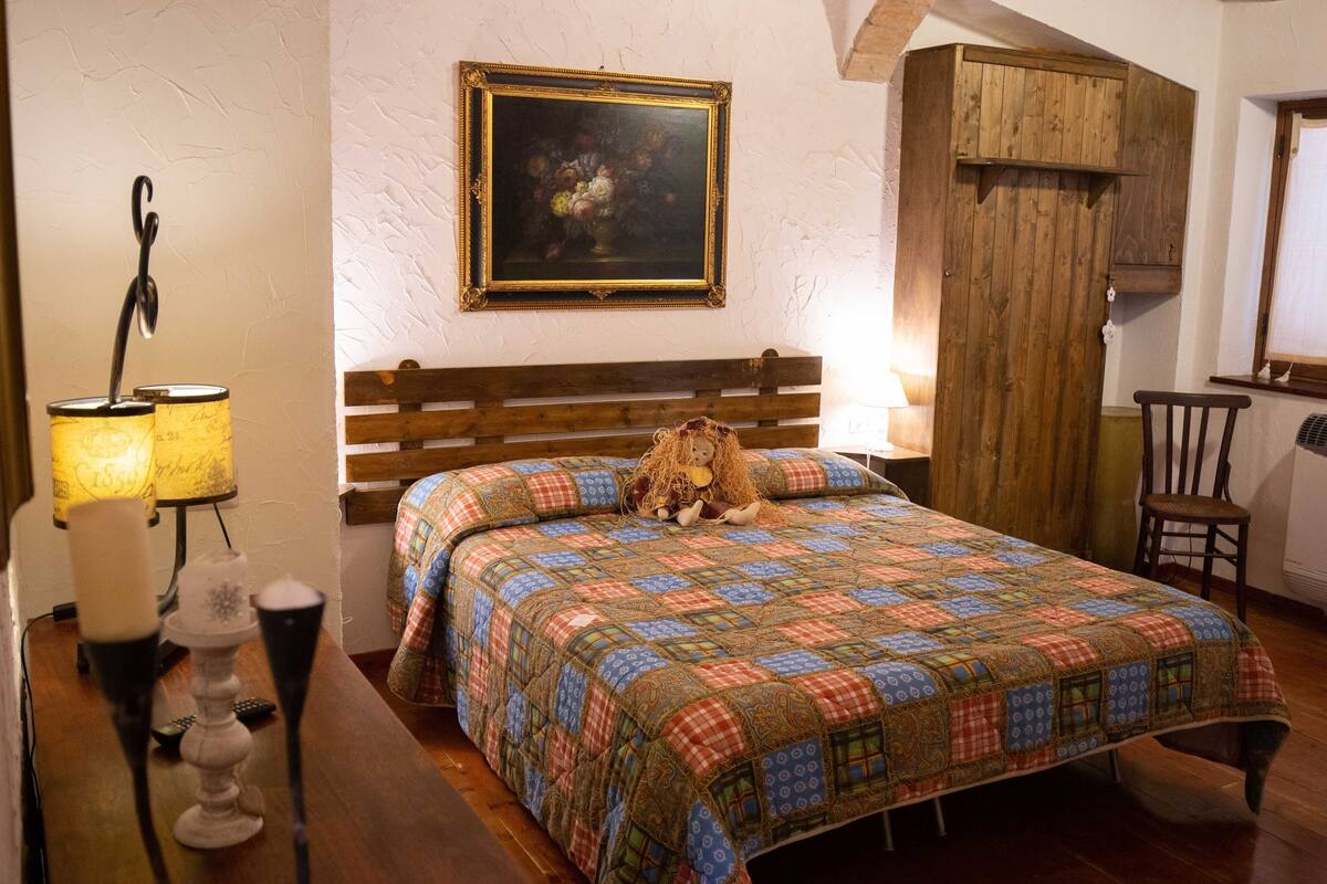 Un dormitorio con una cama de madera, una colcha, un cuadro en la pared y un armario de madera.