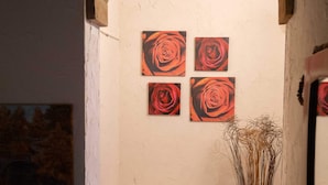 Un pasillo estrecho con un arco de entrada a una habitación. La habitación tiene un aparador blanco con cuatro cajones y un jarrón con plantas secas. Hay cuatro cuadros de rosas en la pared.
