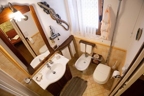 A bathroom with two sinks, a bidet, a toilet, a mirror, a towel rack, and a shower area.