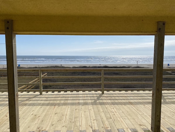 A wooden deck with a view of the beach and ocean.