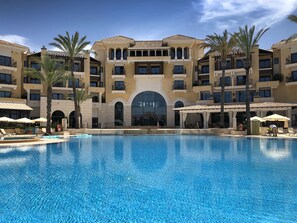 A hotel with a large swimming pool, multiple balconies, and palm trees. - Spacious 3-bed, 2-bath apartment with balcony, frontline golf and lake views (Torre-Pacheco)