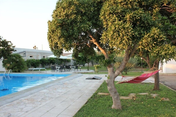 Une piscine avec un hamac et un arbre au premier plan.