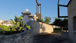 Un patio con muro de piedra, plantas de cactus y una escultura de metal.