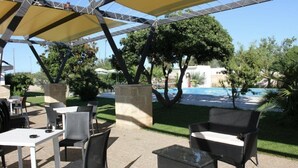 Un patio exterior con mesas y sillas, una piscina y vistas al océano.