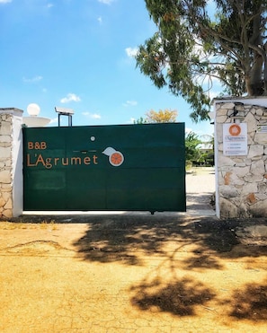 Une porte verte portant l’inscription « B&B L’agrume » et un logo représentant un agrume, indiquant qu’il s’agit d’un établissement proposant des chambres d’hôtes et mettant l’accent sur les agrumes.